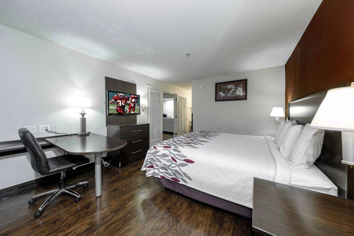 A hotel room with a bed, desk, chair, TV, and a painting on the wall.