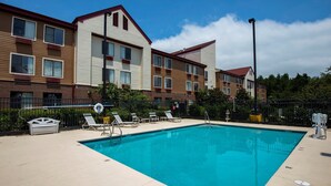 A swimming pool with lounge chairs and a fence, surrounded by multi-story buildings.