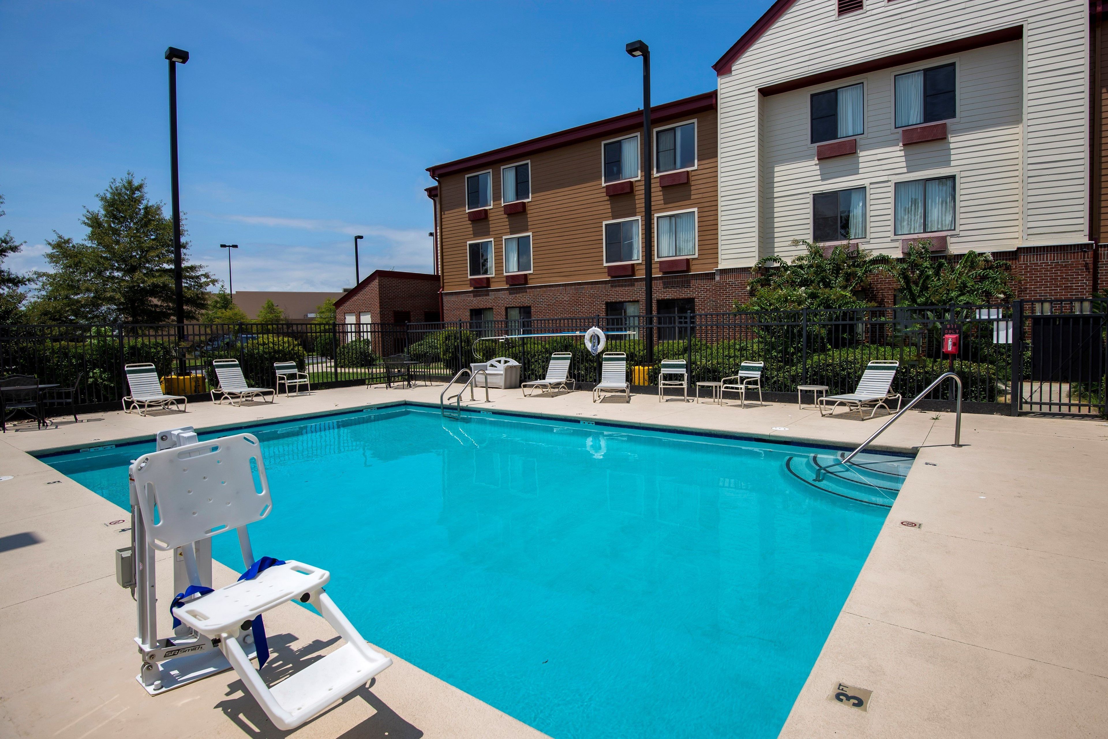 A swimming pool with a lifeguard chair, lounge chairs, and a fence.