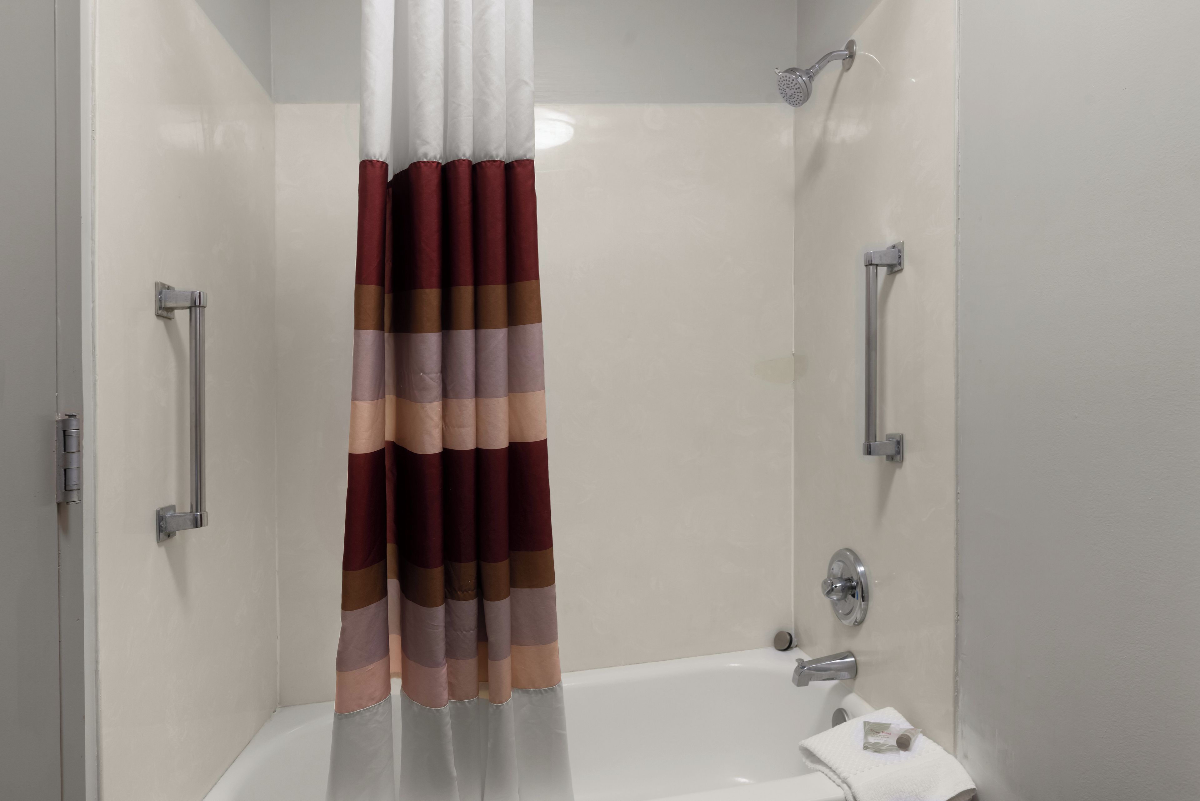 Une douche avec un rideau à rayures, un pommeau de douche à main et une serviette blanche sur le sol.
