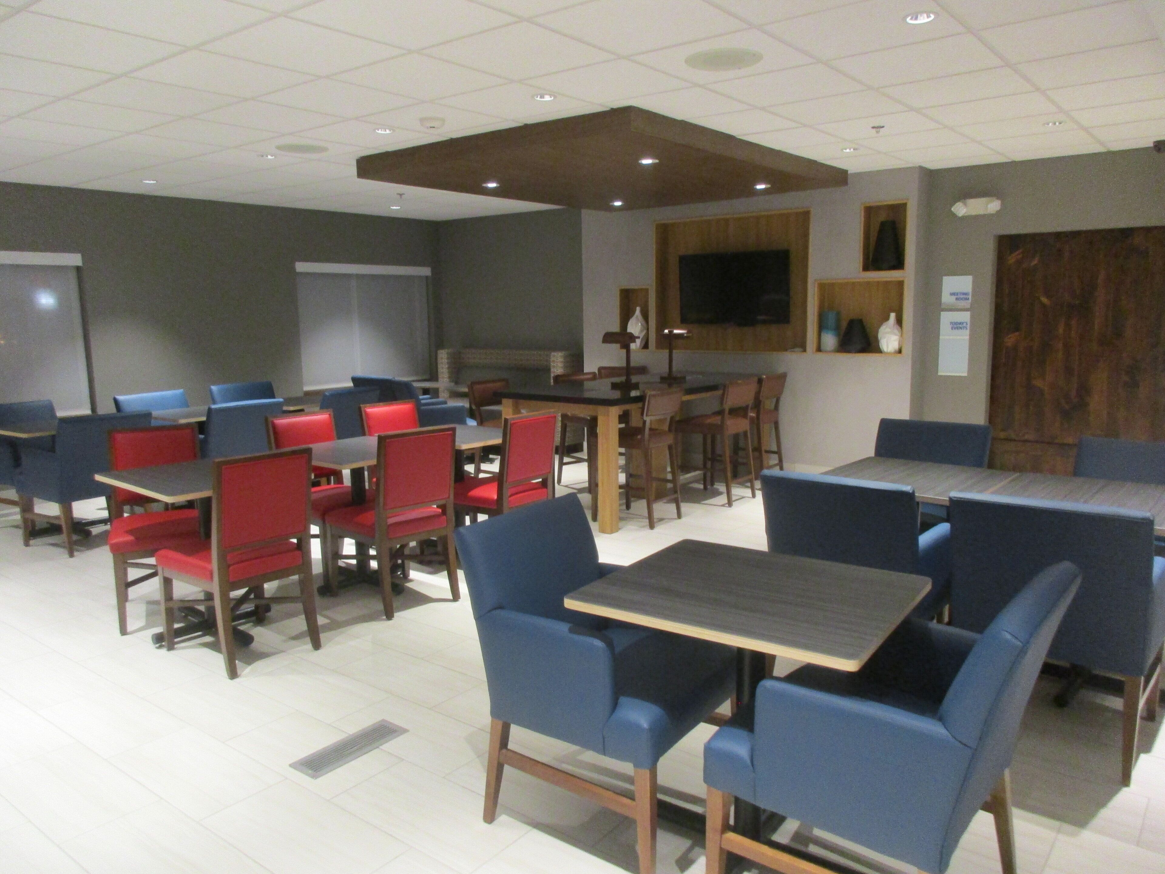 A conference room with multiple tables and chairs, a large screen, and a wooden accent wall.
