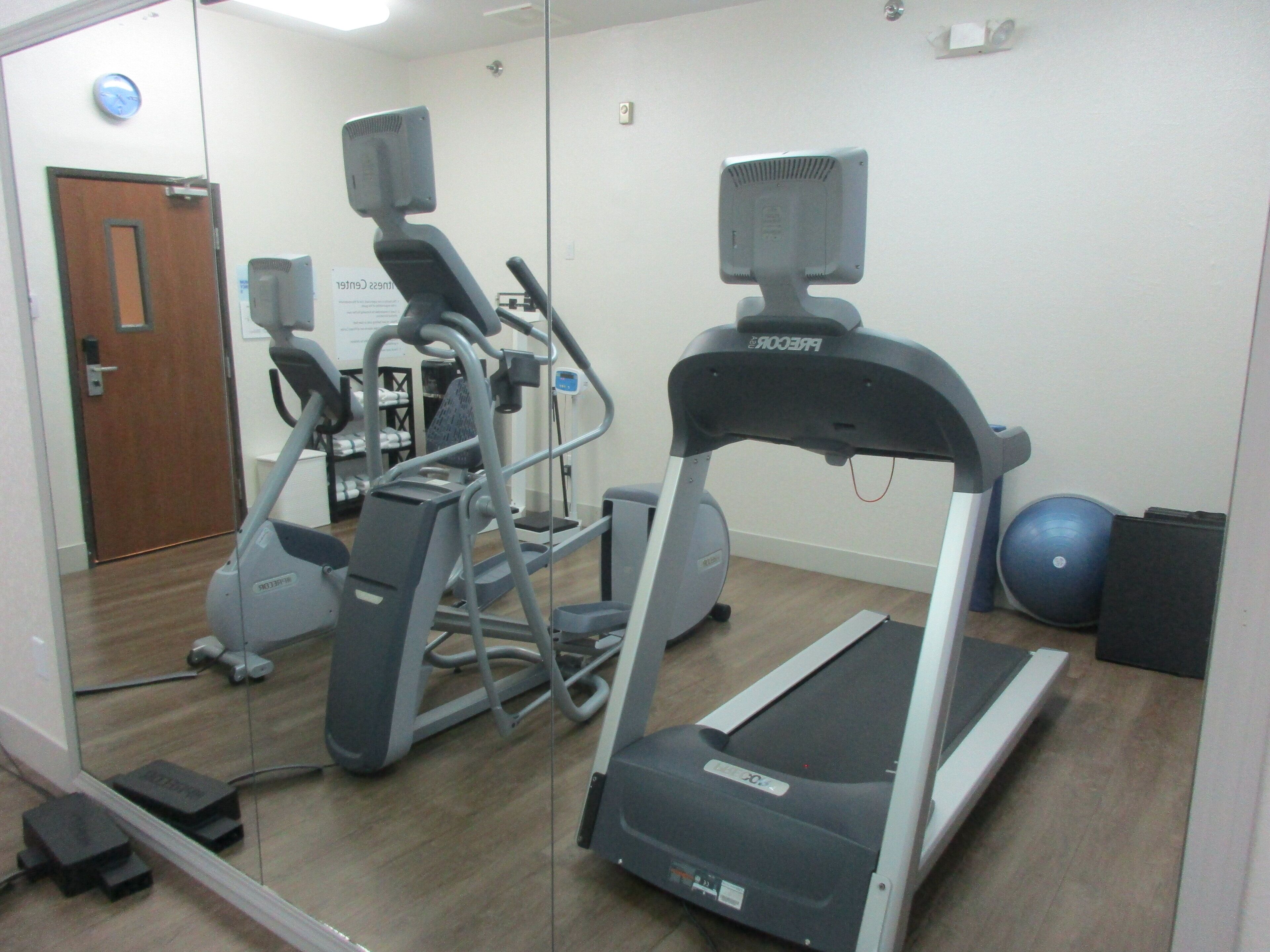 A gym with exercise equipment including a treadmill, elliptical, and weights.