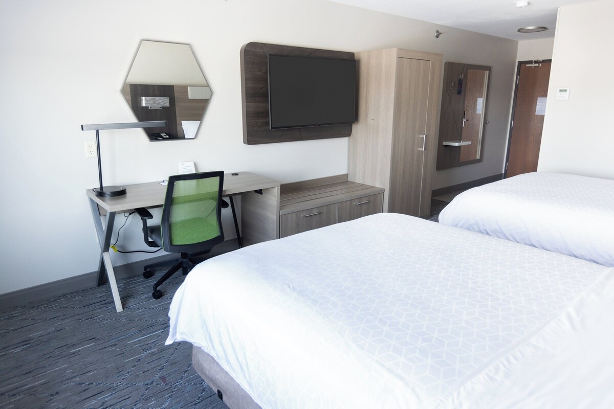A hotel room with two beds, a desk with a chair, a flat-screen TV mounted on the wall, and a wardrobe.