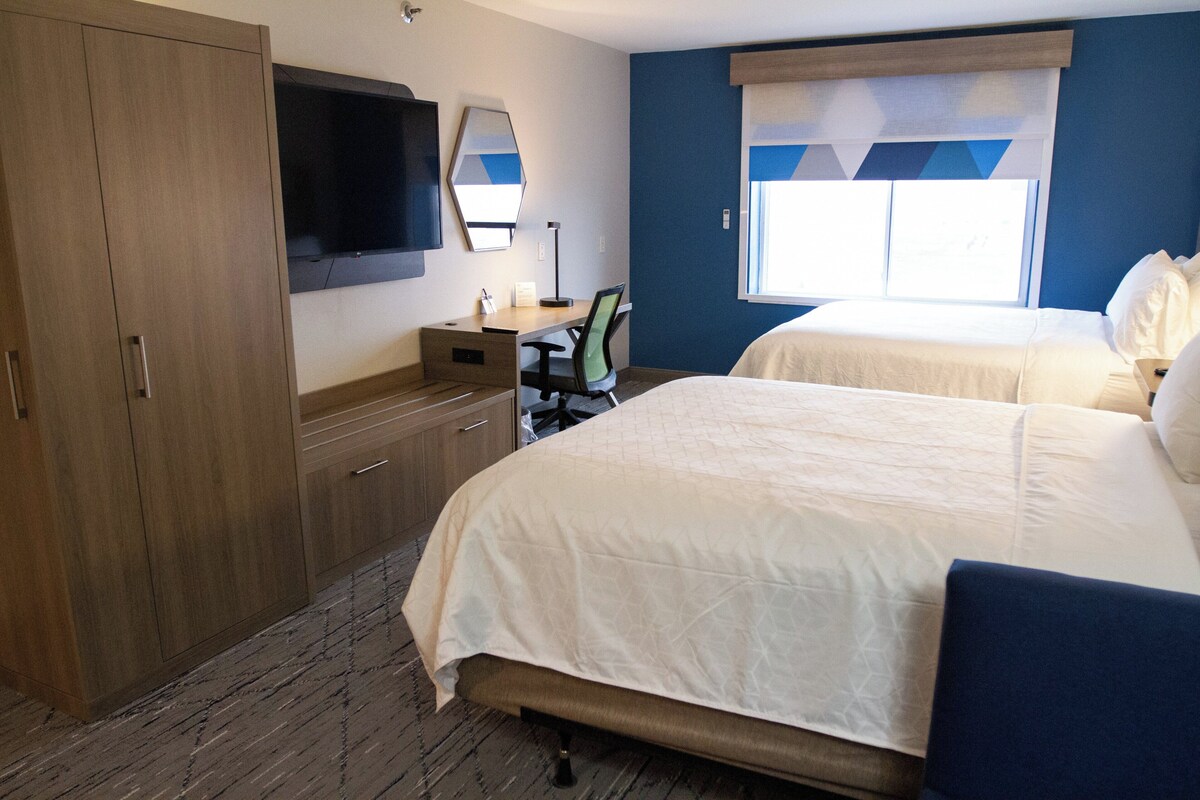 A hotel room with a large wardrobe, a desk with a chair, a bed, and a television mounted on the wall.