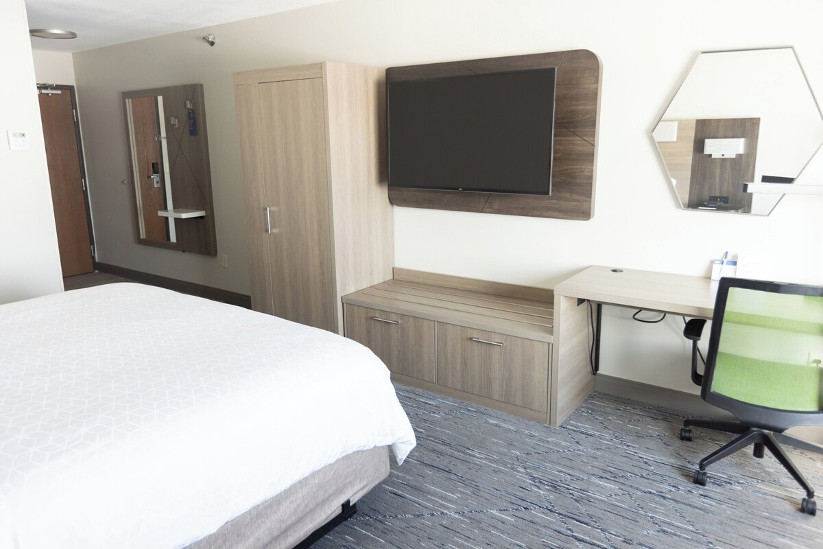 A hotel room with a bed, a desk, a chair, a TV, a wardrobe, and a mirror.