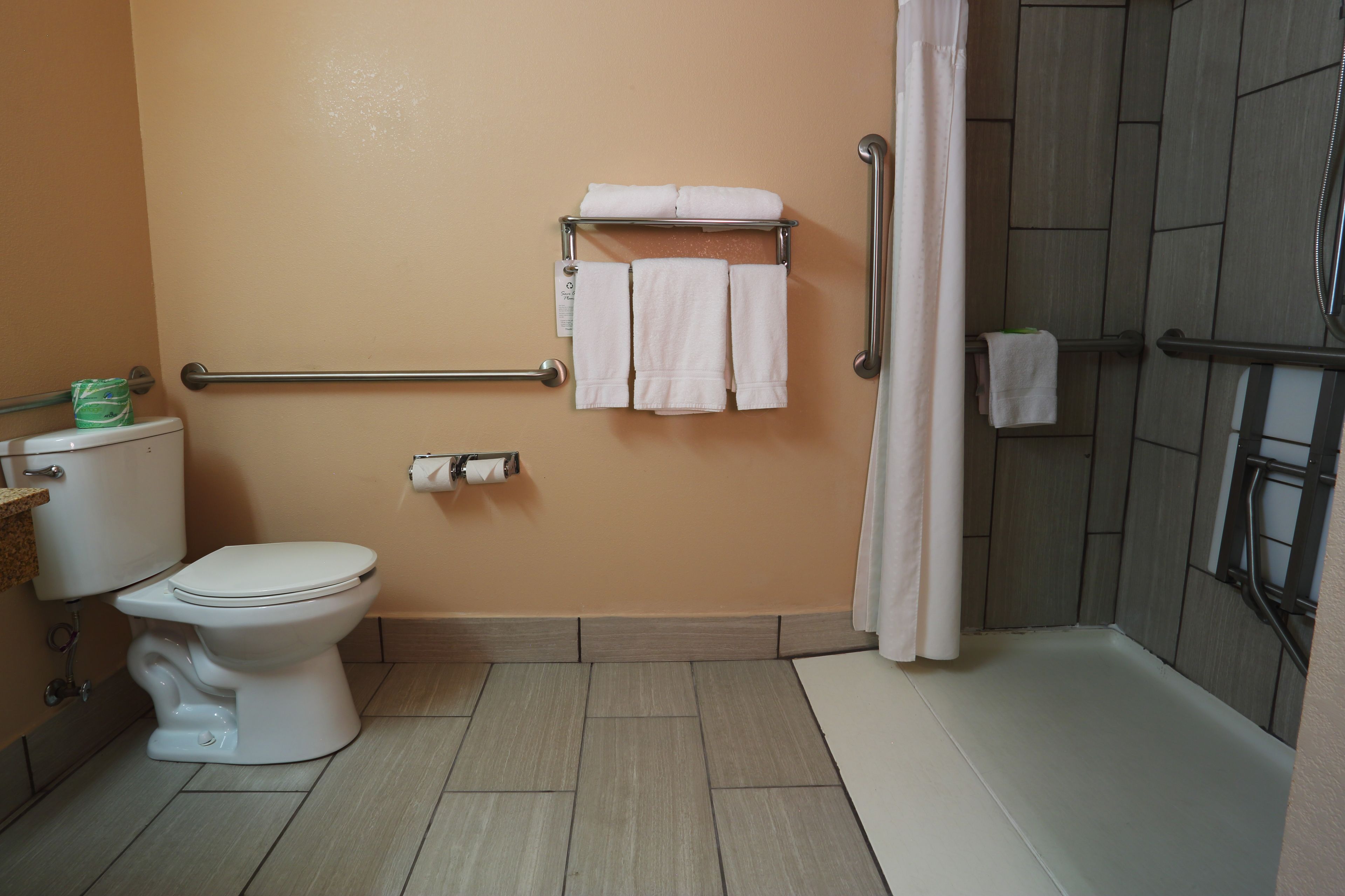 A bathroom with a toilet, a towel rack with towels, a shower area, and a toilet paper dispenser.