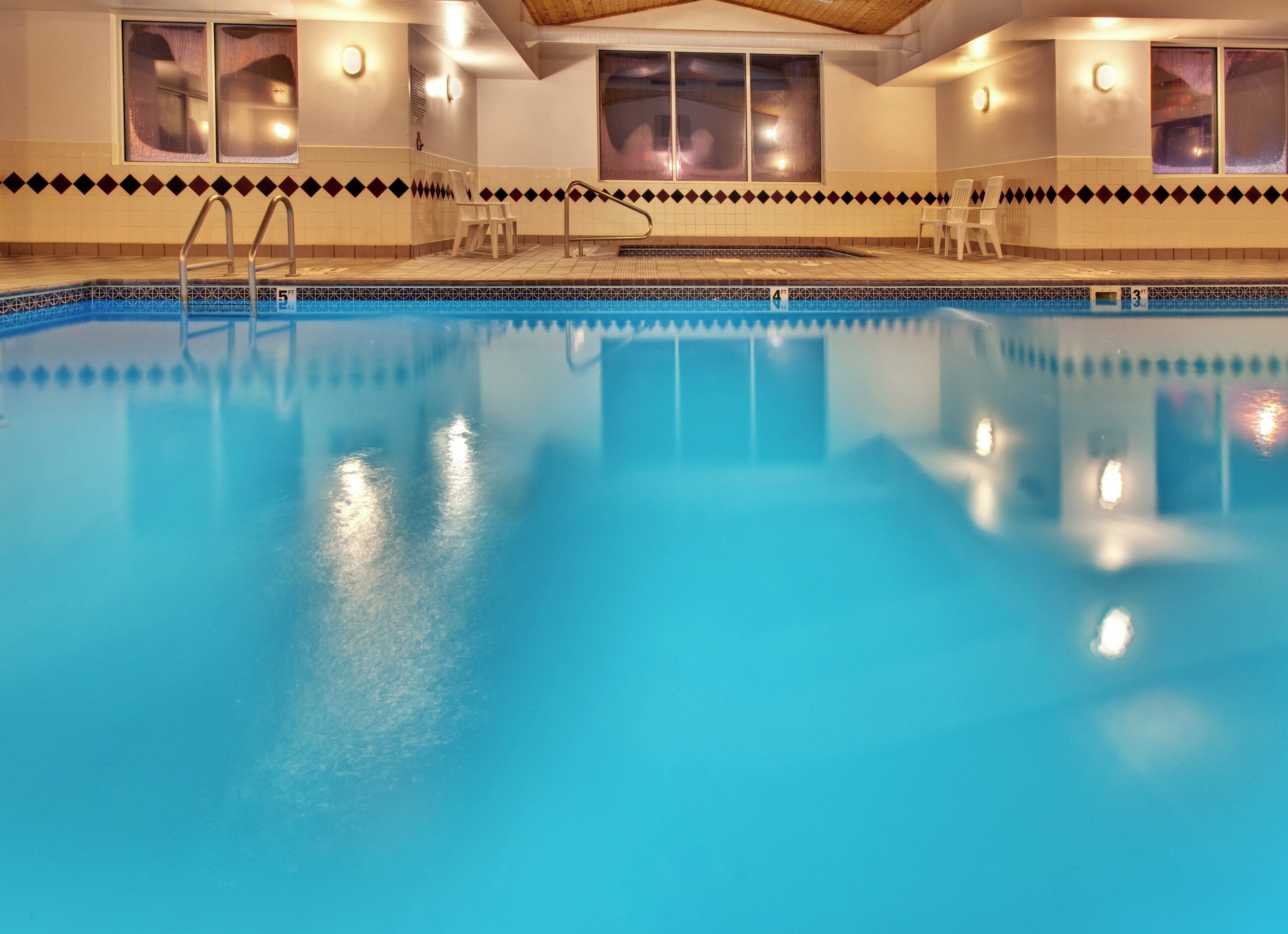 An indoor swimming pool with clear water, surrounded by tiled walls and windows.