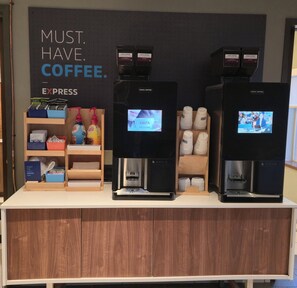 A coffee station with three espresso machines, a display of coffee pods, and a sign that reads "MUST. HAVE. COFFEE."