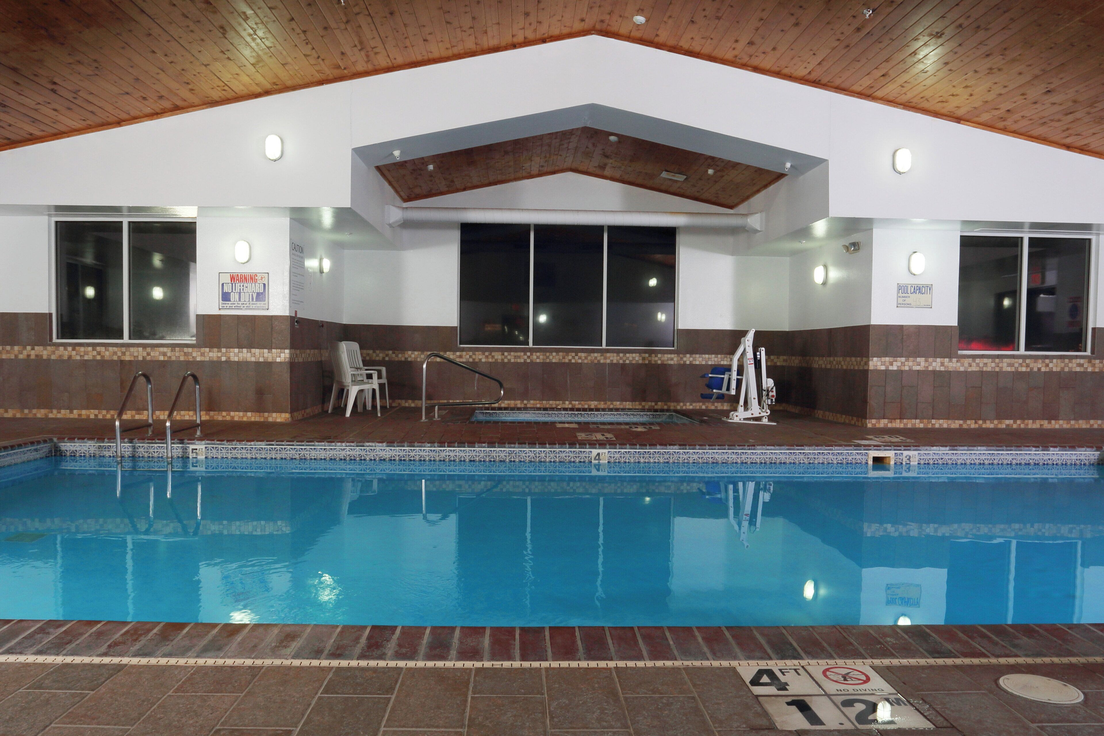 An indoor swimming pool with a tiled floor, a wooden ceiling, and a lifeguard station.