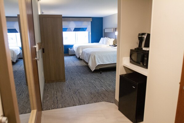 A hotel room with two beds, a coffee machine, and a small refrigerator.