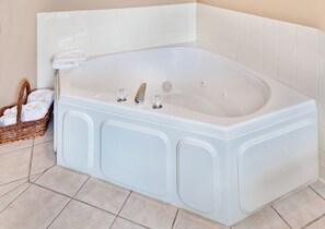 A large white bathtub with a built-in seat, a control panel with three knobs, and a small basket of folded towels on the floor beside it.