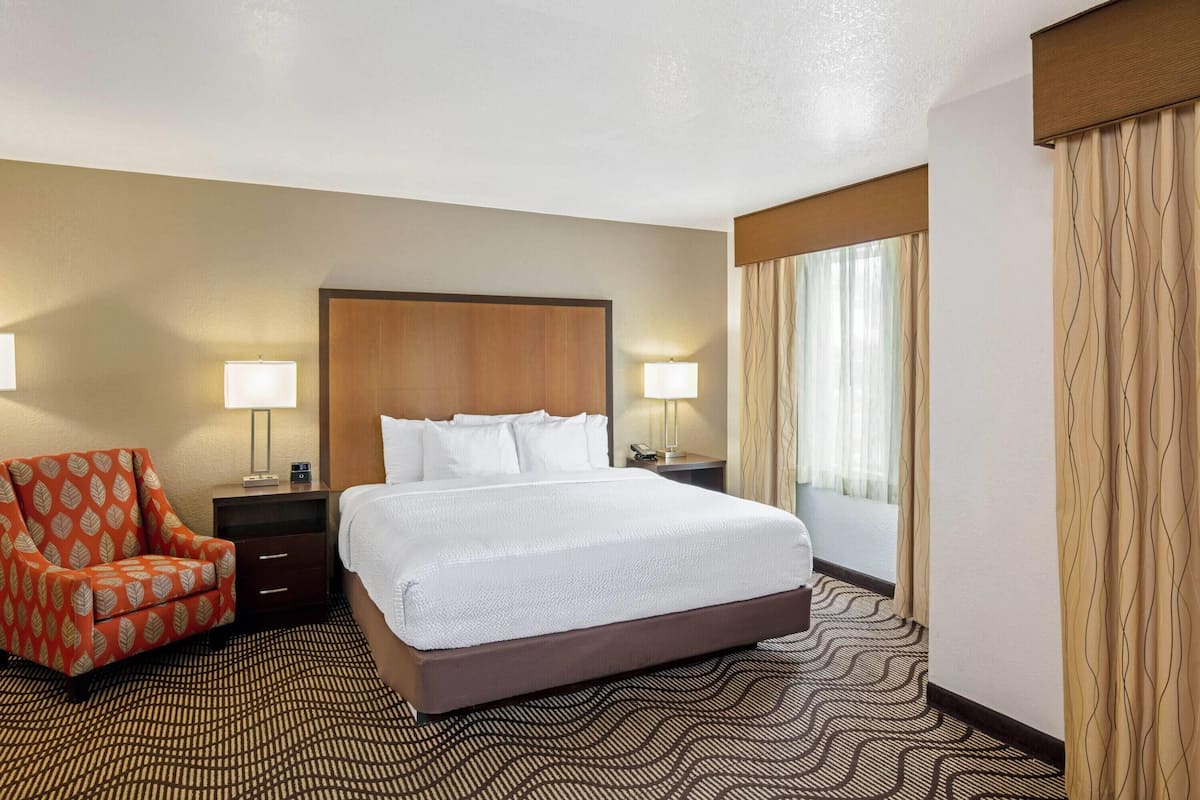 A hotel room with a large bed, a chair, a nightstand, and a window with curtains.