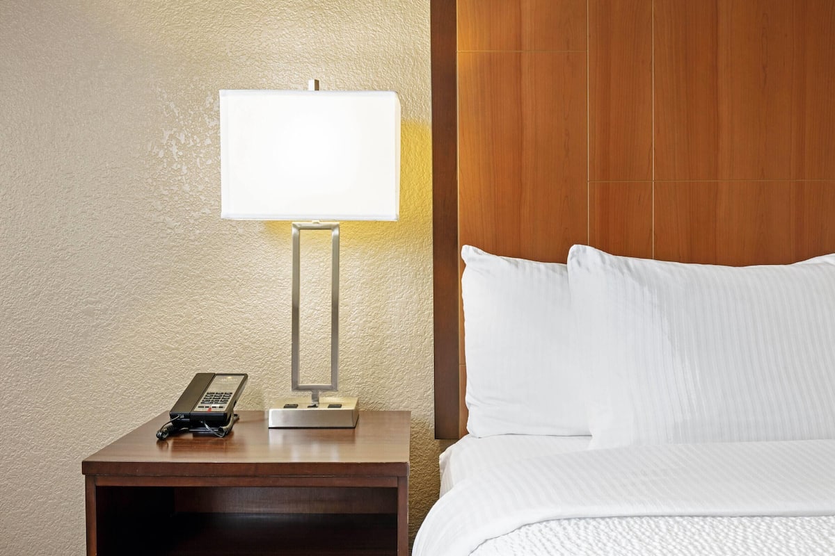 A hotel room with a wooden headboard, a bedside table with a lamp, a telephone, and a neatly made bed.