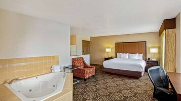 A hotel room with a large bed, a sitting area with a chair, a desk, a bathroom with a bathtub, and a patterned carpet.