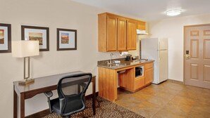 A compact kitchen with wooden cabinets, a countertop, a sink, a refrigerator, and a dining area with a chair and table. - La Quinta Inn & Suites by Wyndham Las Vegas Red Rock (Las Vegas)