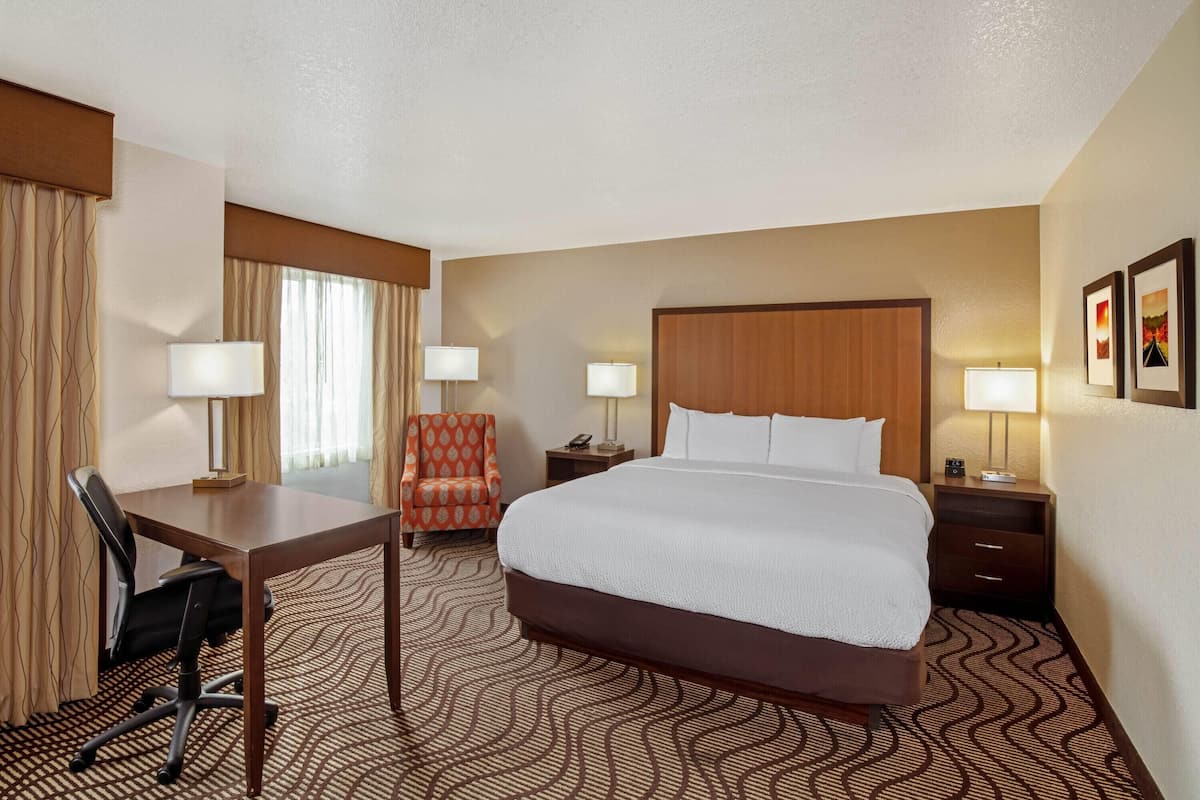 A hotel room with a large bed, a desk with a chair, two bedside lamps, and a telephone.
