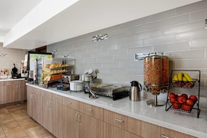 A kitchen area with a coffee machine, a bread display, a fruit basket, and a juice dispenser. - La Quinta Inn & Suites by Wyndham Las Vegas Red Rock (Las Vegas)