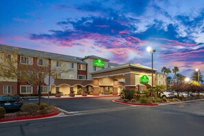 Un hotel con un cartel de 'La Quinta', un estacionamiento y un cielo despejado con nubes.