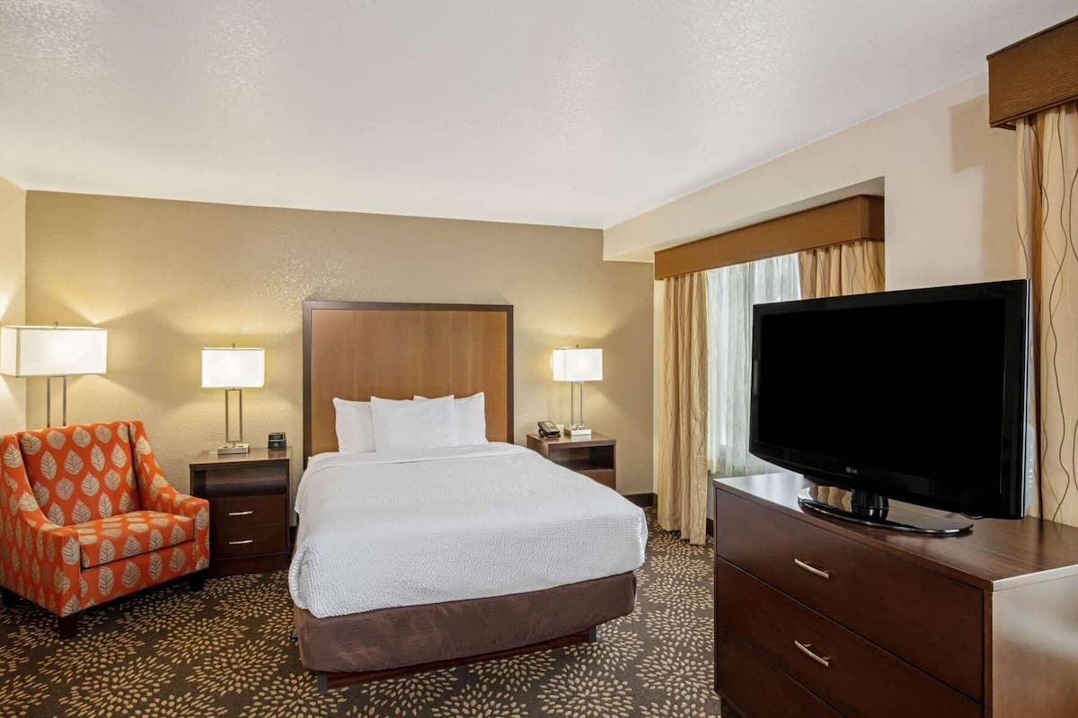 A hotel room with a bed, a TV, a chair, and a desk.
