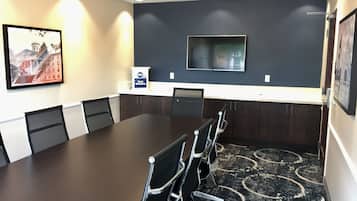 Un salón de conferencias con una larga mesa, sillas, un televisor y un cartel que indica alojamiento Best Western.