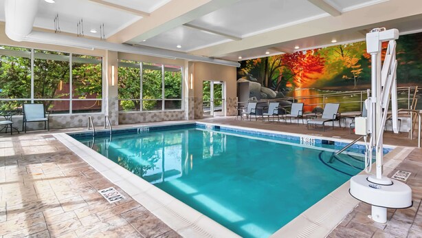 An indoor swimming pool with clear water, surrounded by lounge chairs and a mural of autumn trees. - Best Western Gettysburg (Gettysburg)