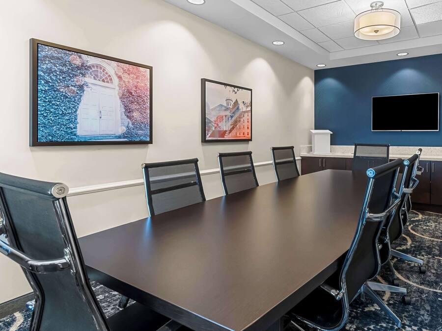 A conference room with a long table, six chairs, and a TV on the wall.