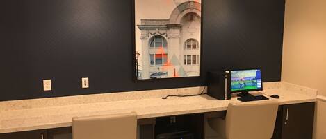 A modern office space with a dark wall, a framed picture, a desktop computer, and two office chairs.