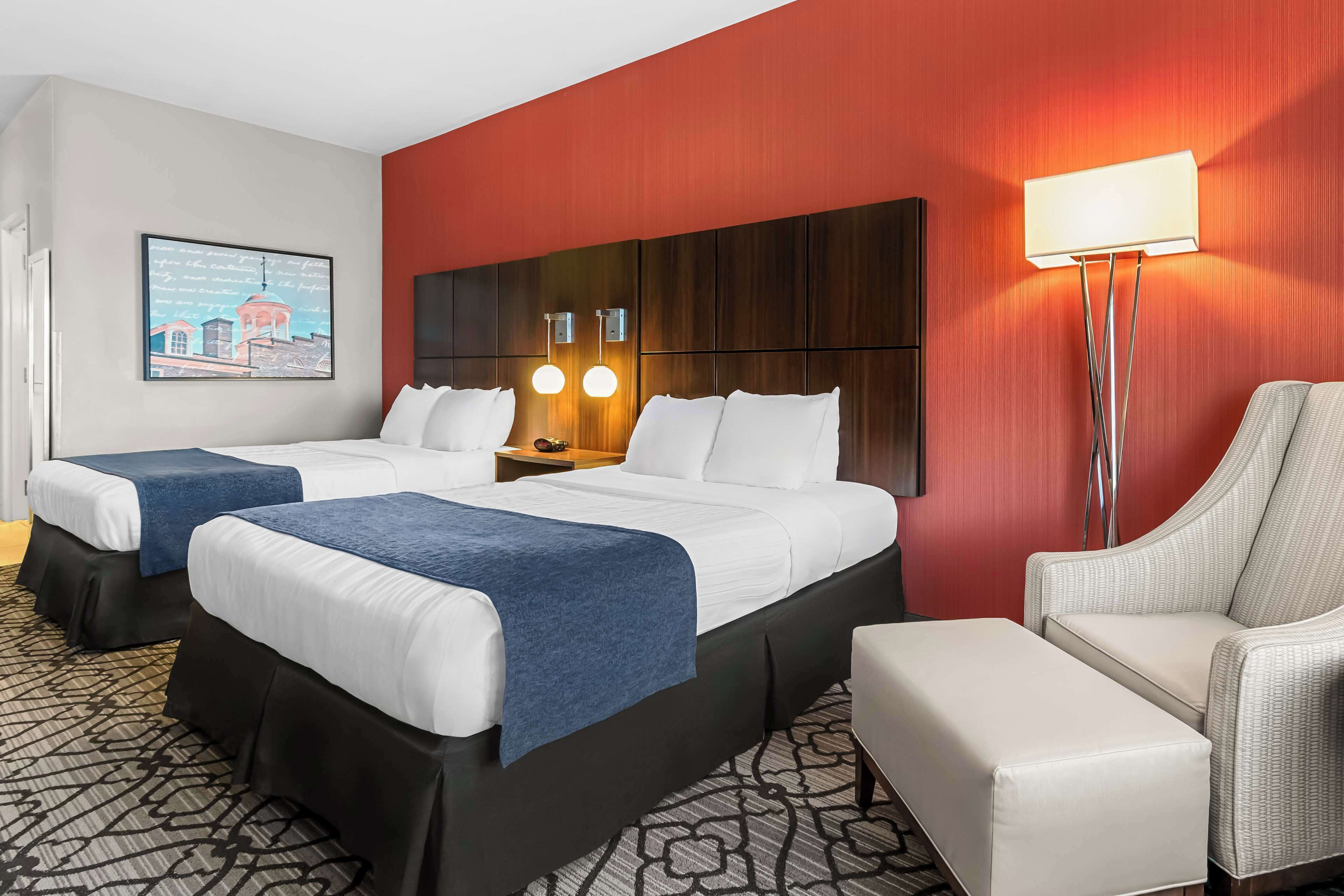 A hotel room with two beds, a desk, a chair, and a lamp.