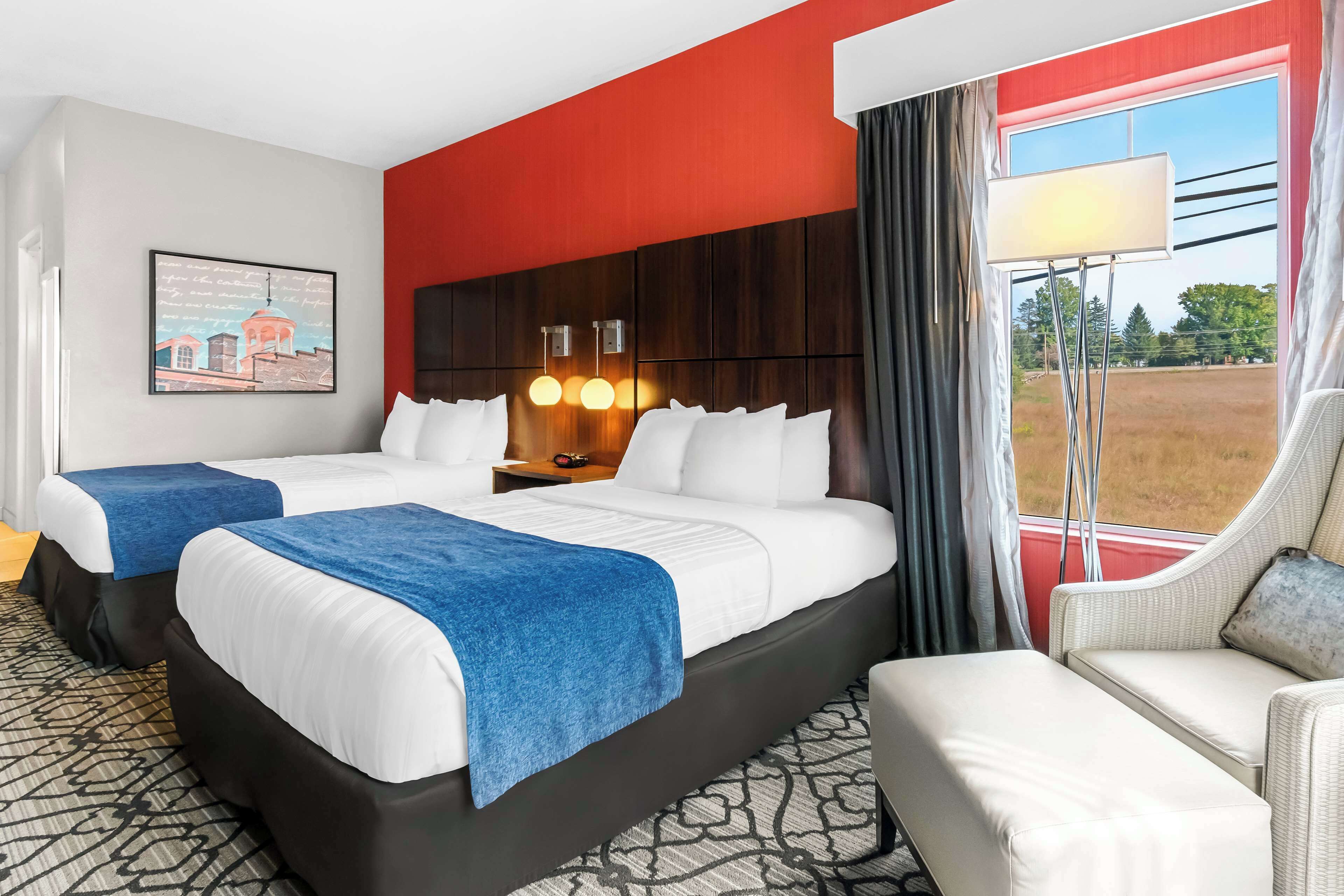 A hotel room with two beds, a sofa, a large window with a view, and a painting on the wall.