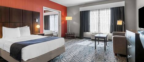 A hotel room with a large bed, a desk, a chair, a dresser, and a TV.