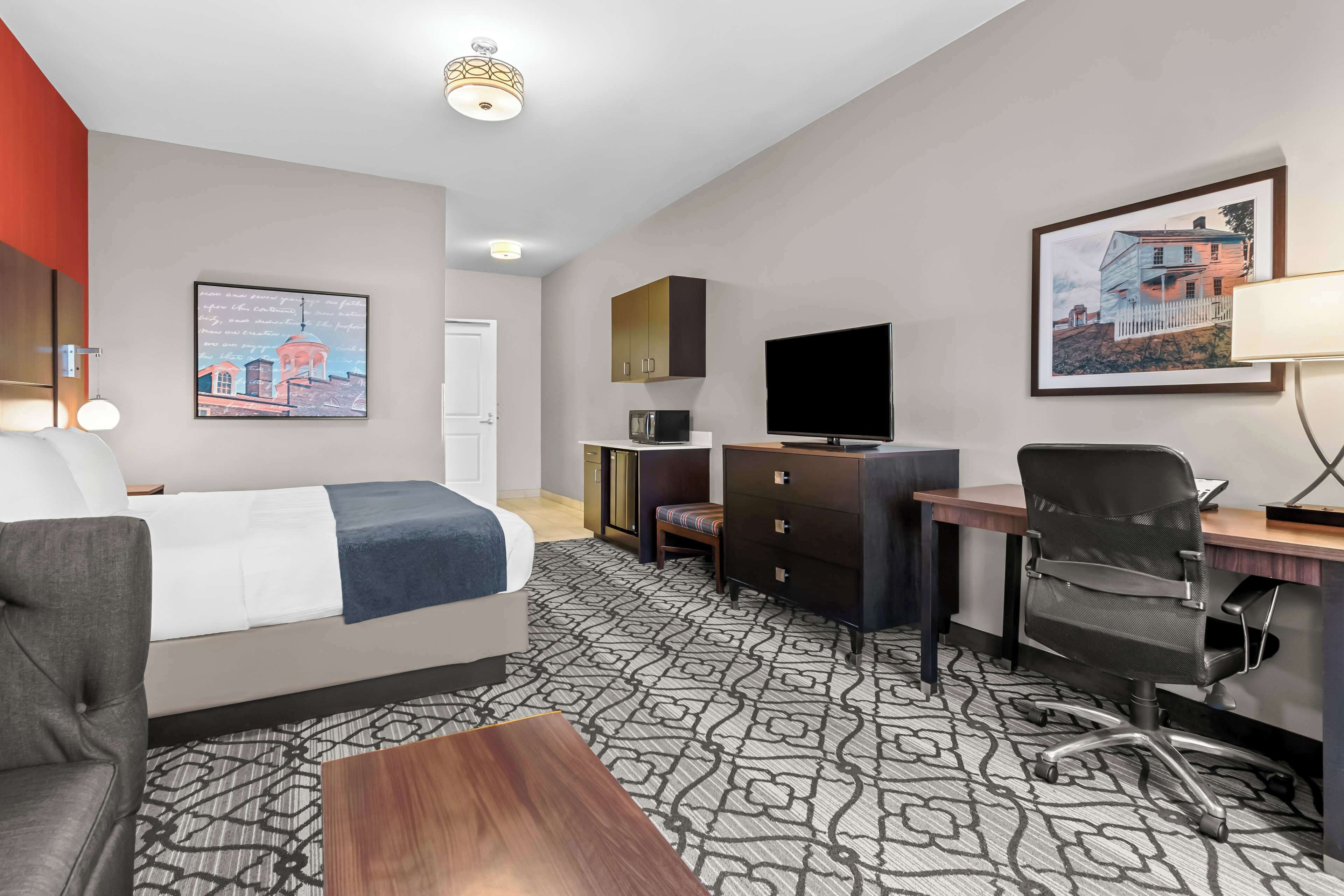 A hotel room with a bed, a desk, a chair, a TV, a wardrobe, and a patterned carpet.