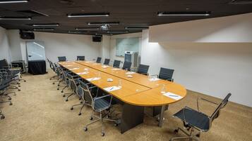 Une salle de conférence équipée d’une longue table, de chaises, d’un projecteur et d’un tableau blanc.