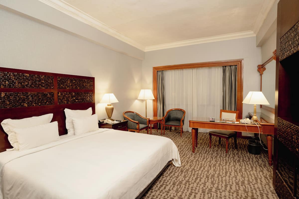 A hotel room with a large bed, two chairs, a desk, and a television.