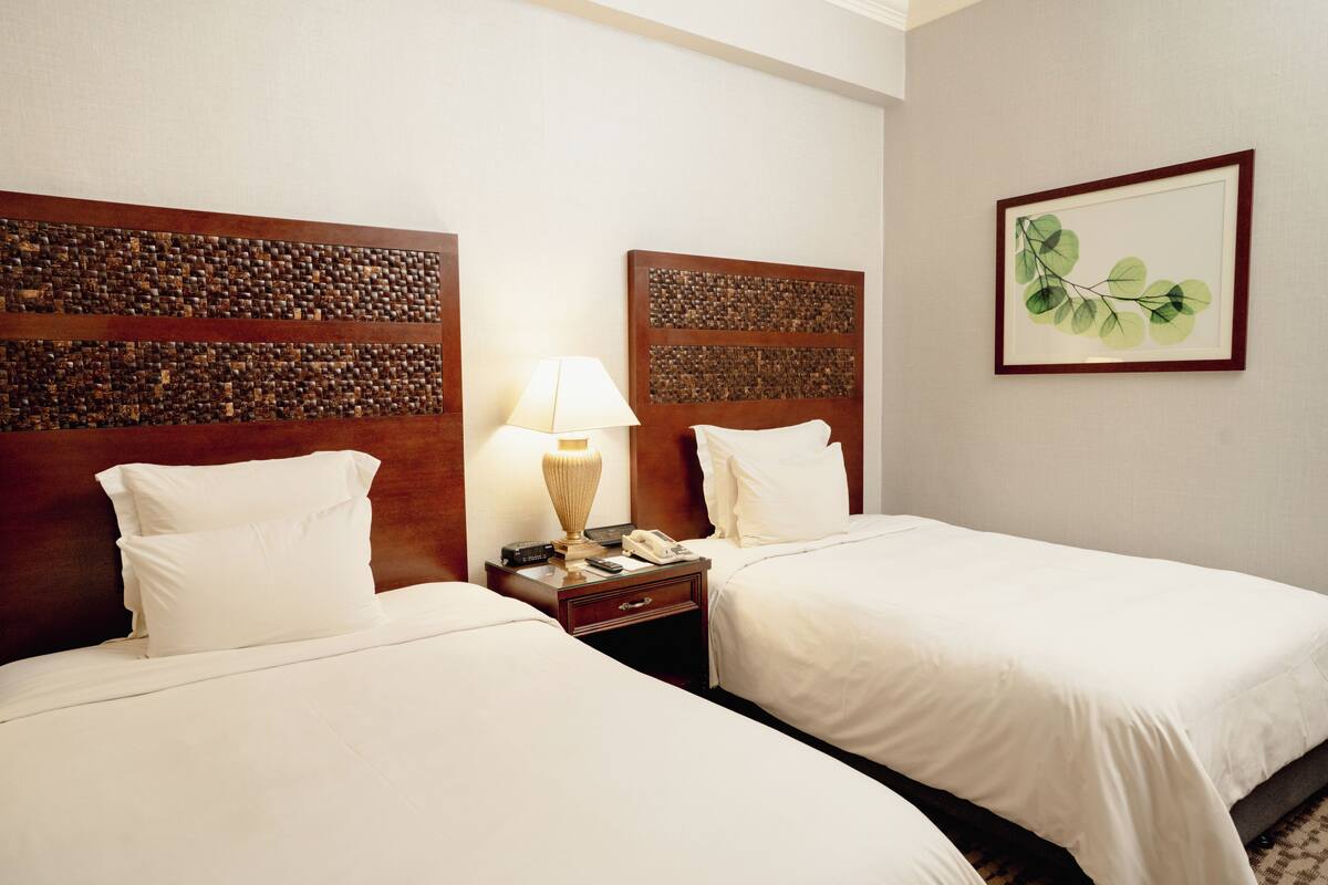 A hotel room with two beds, a nightstand with a lamp, a framed picture on the wall, and a wooden headboard.