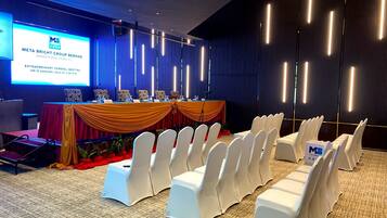 A conference room with a stage, white chairs, and a presentation screen.