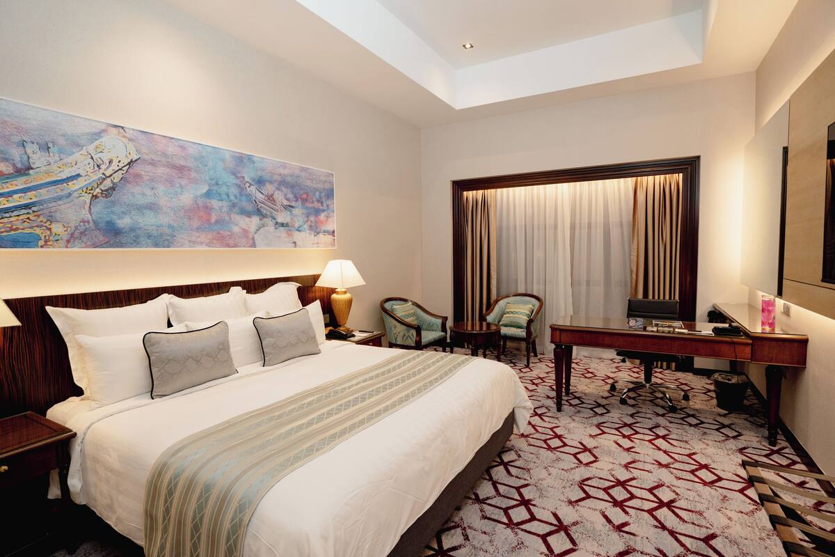 A hotel room with a large bed, a desk, a chair, a TV, and a painting on the wall.