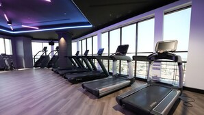 Une salle de sport équipée de plusieurs tapis de course, d’un appareil de marche en escalier et d’une rangée de vélos d’exercice.