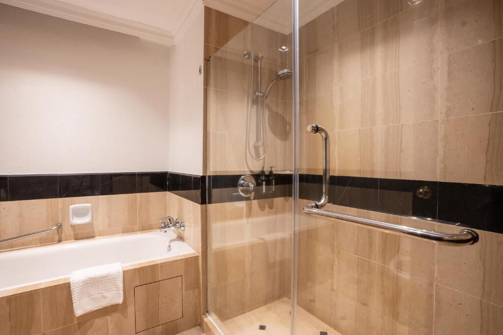 Un bagno moderno con doccia vetrata, vasca da bagno con mancorrente e lavandino bianco.