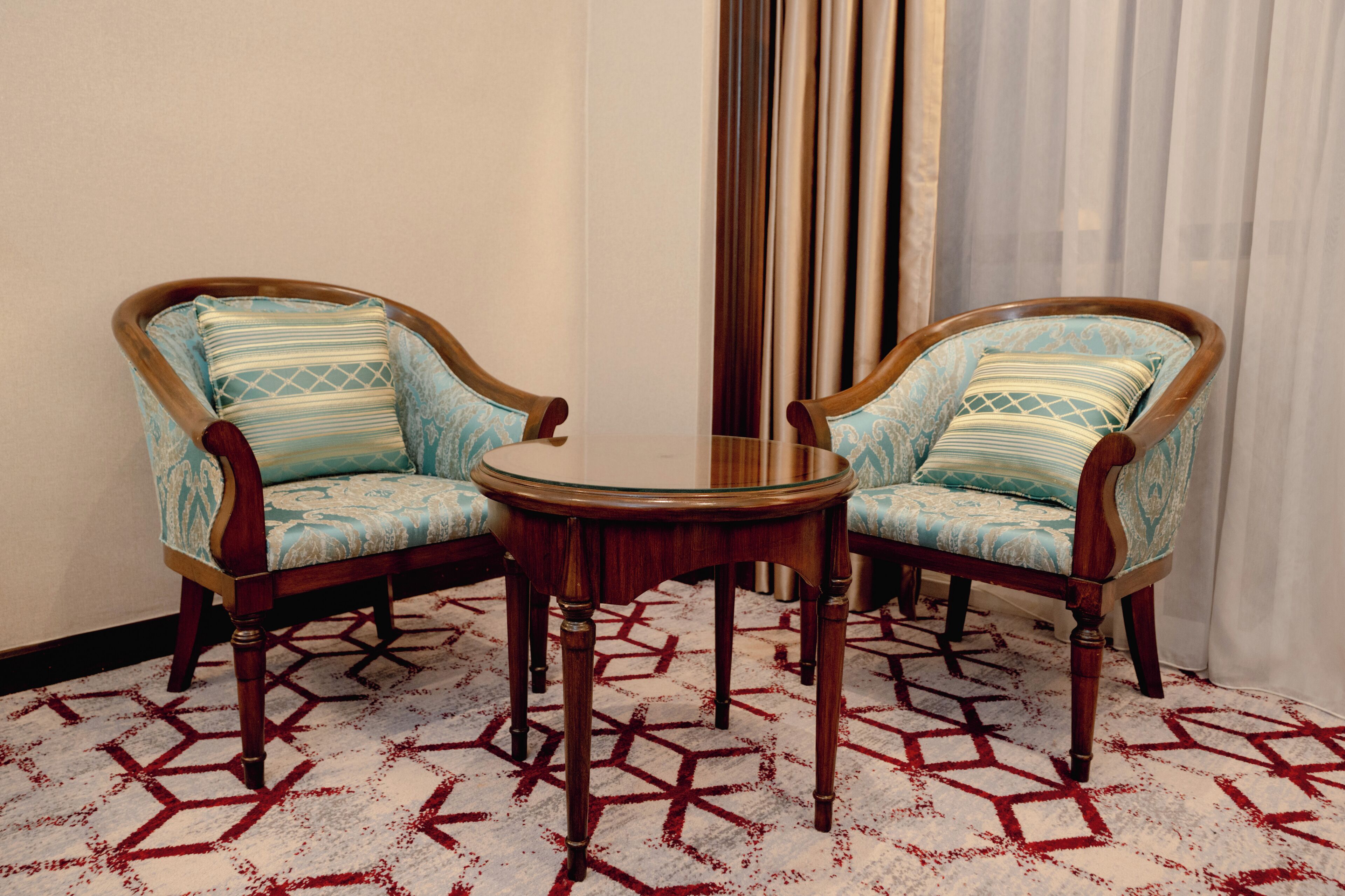 Two upholstered chairs with wooden frames and a small round table between them.