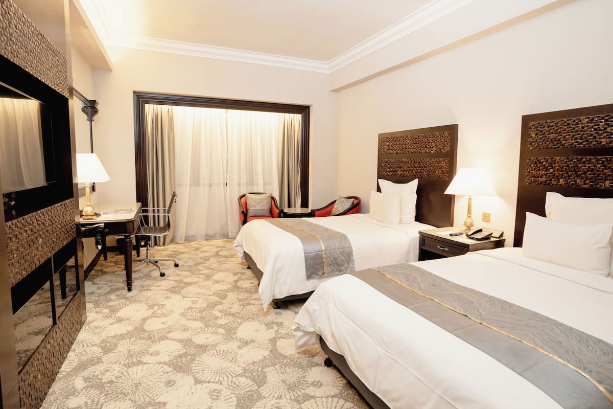 A hotel room with two beds, a desk, and a chair.
