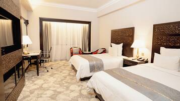 A hotel room with two beds, a desk, and a chair.