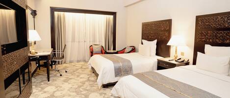 A hotel room with two beds, a desk, and a chair.