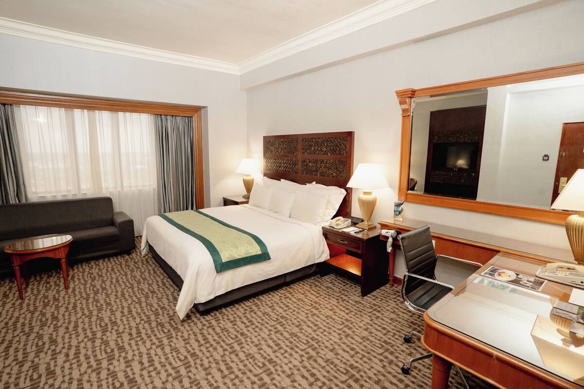 A hotel room with a bed, a desk, a chair, a sofa, and a large mirror.