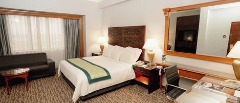 A hotel room with a bed, a desk, a chair, a sofa, and a large mirror.