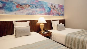 Quarto de hotel com duas camas, mesa de cabeceira com abajur e uma grande pintura abstrata na parede.