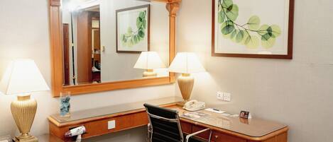 Habitación de hotel con un escritorio de madera, dos lámparas, una silla, un espejo y cuadros en la pared.