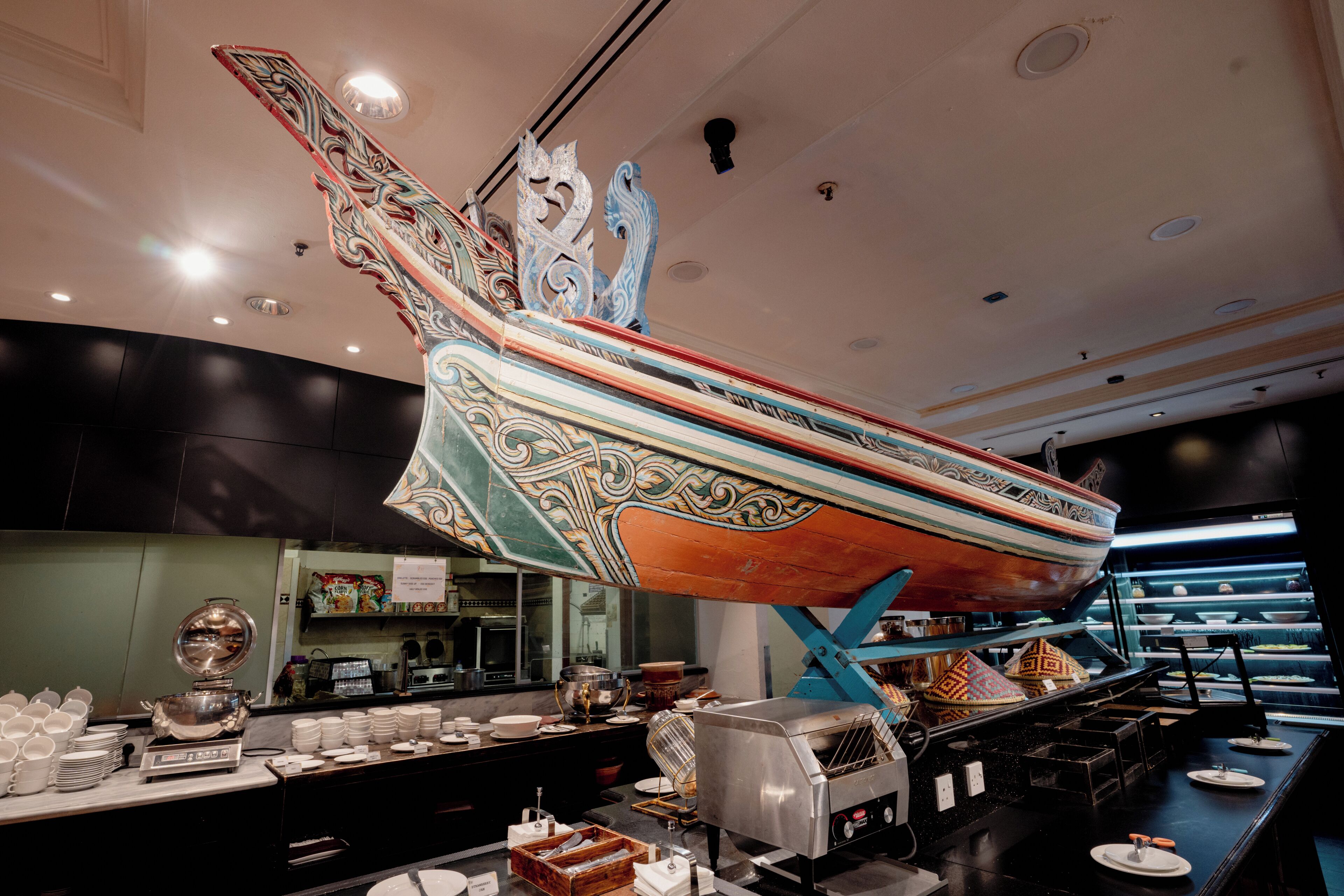 A buffet area with a decorative boat centerpiece, a coffee machine, and various food items on display.