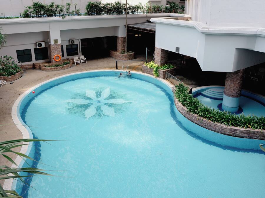 An indoor swimming pool with a star-shaped design, surrounded by plants and a covered area with seating.