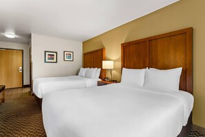 A hotel room with two beds, a wooden headboard, a nightstand with a lamp, and two framed pictures on the wall.