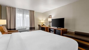 A hotel room with a large bed, a desk with a flat-screen TV, a chair, a sofa, and a window with curtains.